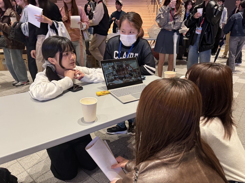 パソコンを置いたテーブルを挟み、活動について話す学生たち