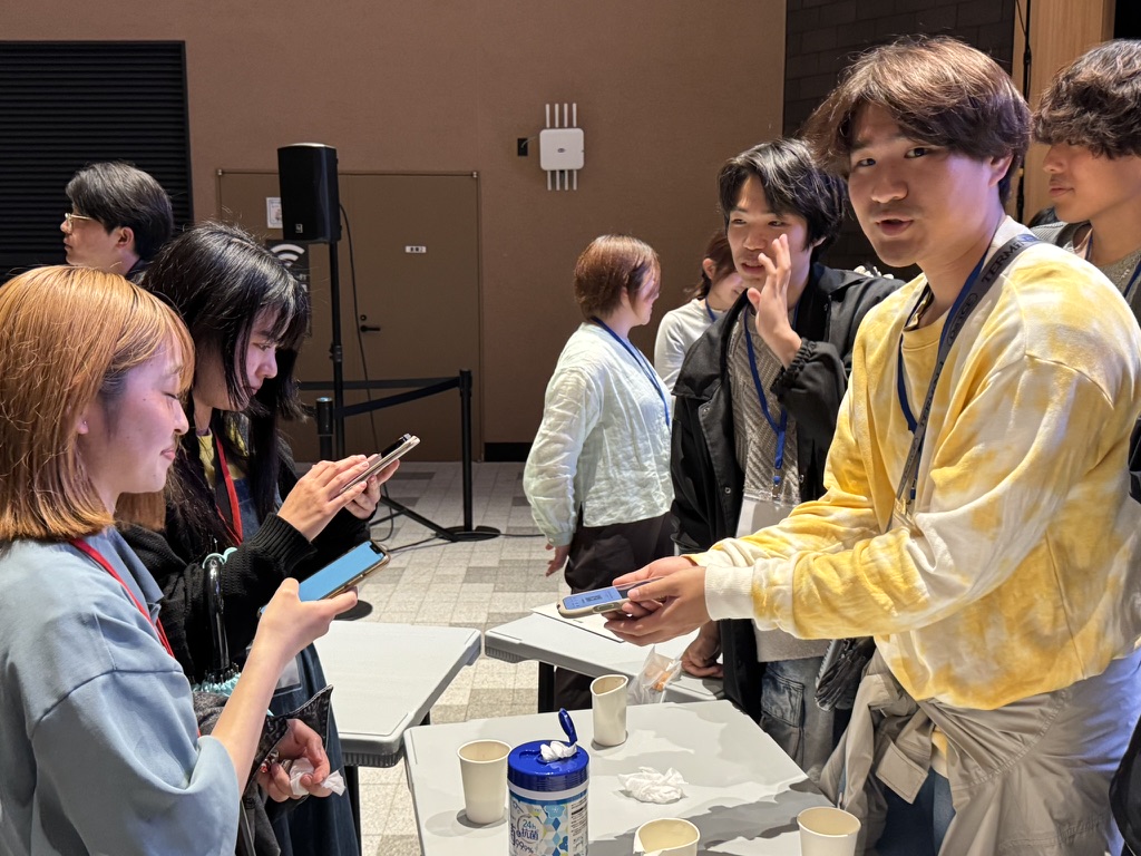 テーブルの前で資料やスマートフォンを手に交流する学生たち